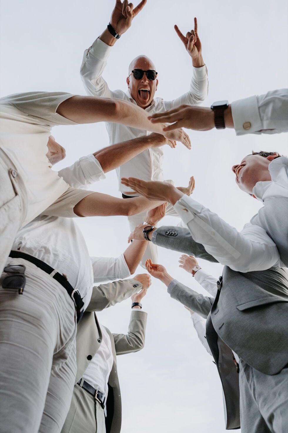 Mehrere Gäste werfen den Bräutigam jubelnd in die Luft, Perspektive von unten aufgenommen.