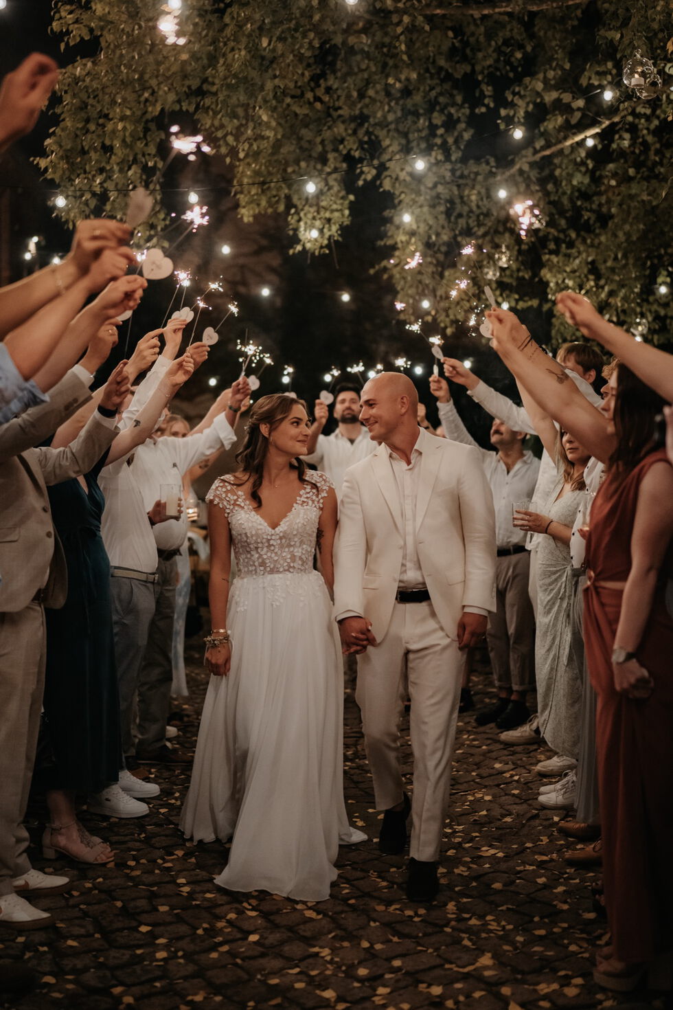 Braut und Bräutigam gehen bei Nacht durch ein Spalier aus Gästen, die Wunderkerzen halten.