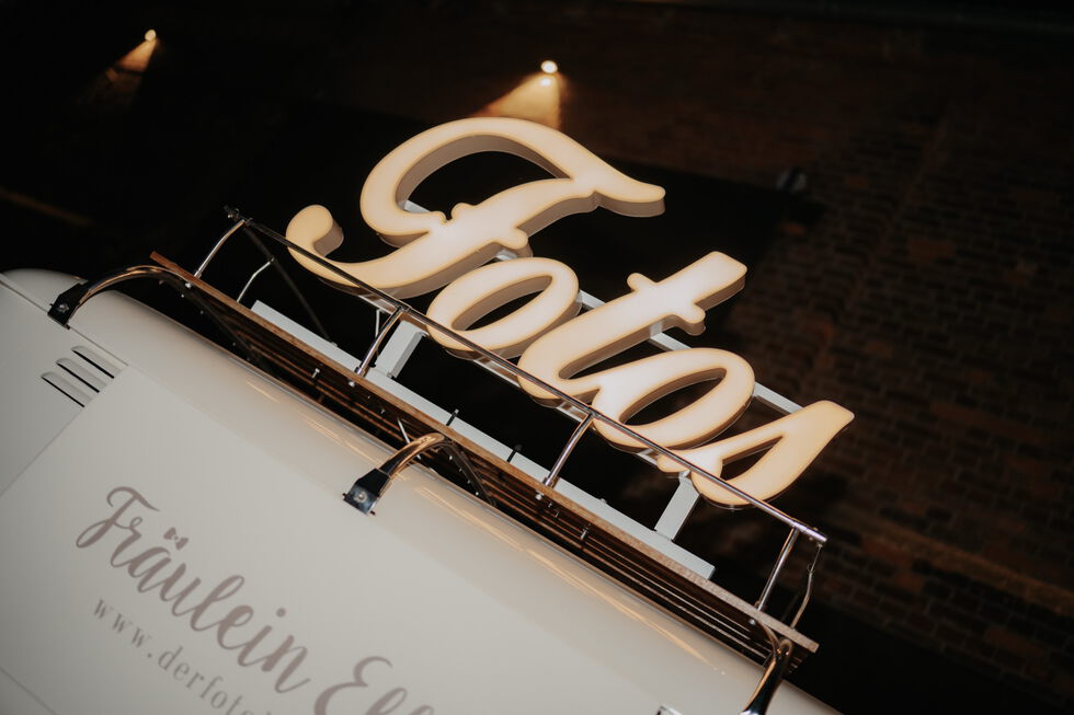 Detailaufnahme eines Foto-Busses mit großem beleuchtetem „Fotos“-Schriftzug auf dem Dach.