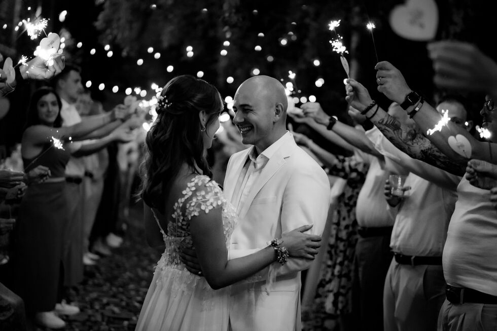 Braut und Bräutigam umarmen sich während eines Wunderkerzenspalieres, umgeben von Gästen.