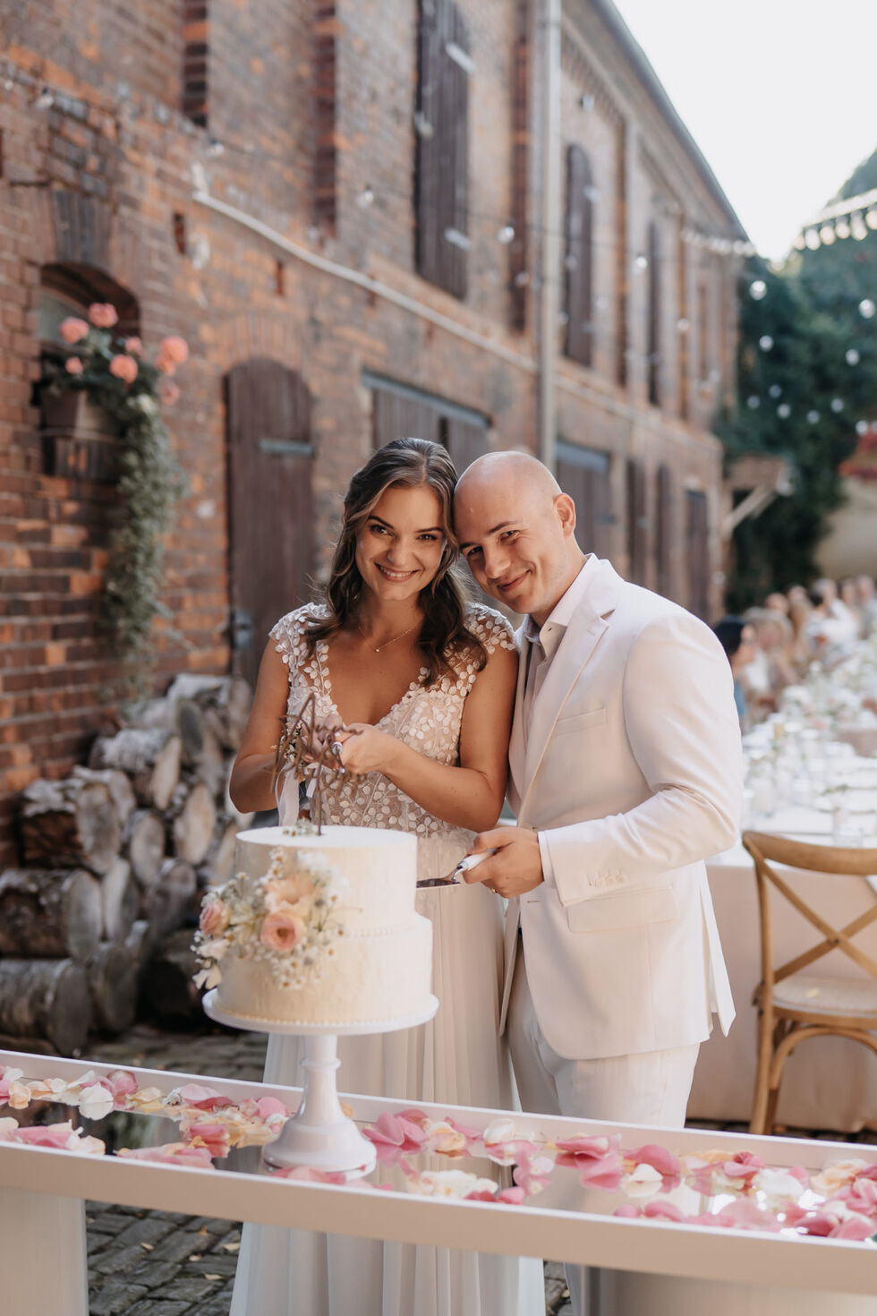 Braut und Bräutigam schneiden gemeinsam ihre zweistöckige weiße Hochzeitstorte an.